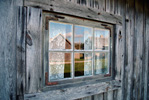 Fönster med spetsgardin på ett trärent, grått och väderbitet hus.